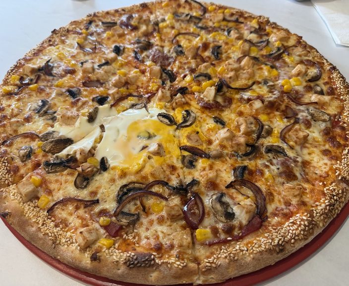 Pizza topped with fried egg, sweetcorn, aubergine and onion on a red tray