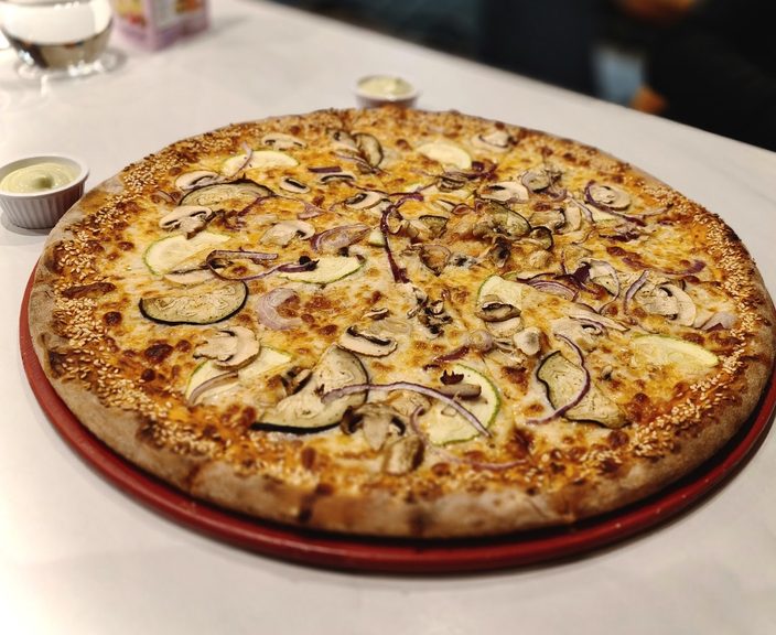 Mushroom and aubergine pizza on a red tray with a pot of dip