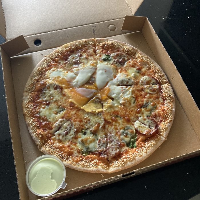 A whole sliced pizza in an open takeaway box with a dip pot