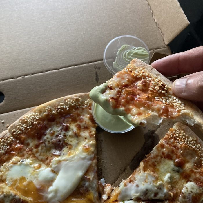 A hand holding a pot of dip over an open box of pizza topped with egg and meat